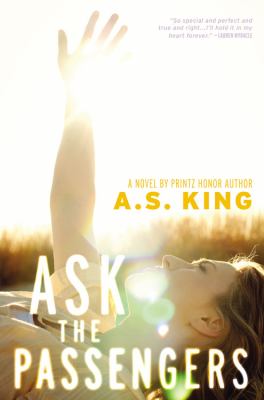 The cover of Ask the Passengers. A teen girl lays on the grass in a field. Sunbeams create solar flares on the cover, obscuring her features. She reaches her hand towards the sky. 